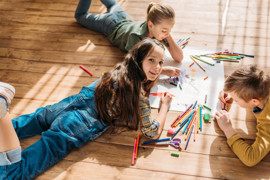 cute kids drawing on paper with pencils while lying on floor