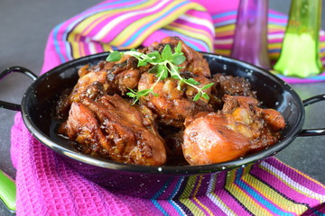 Chicken with prunes cooked in the oven in a black bowl on a textile background