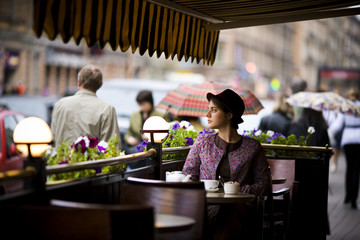 Beautiful young woman in hat with a Cup of tea sitting in a cafe looking at prodasih by people.