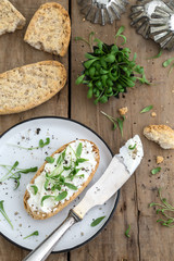 Brötchen mit Frischkäse, Kresse und Pfeffer zusammen mit einem Teller und einem Messer auf einem...