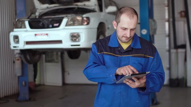 30s car mechanic in blue uniform using tablet in car repair auto service