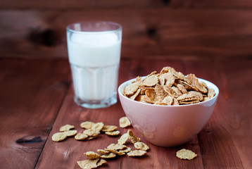Flakes of cereals for breakfast with a glass of milk. Oat flakes in a deep bowl on a wooden table. Flakes with milk.