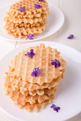 Belgian waffles on white plate on wooden background decorated purple flower. Top view.