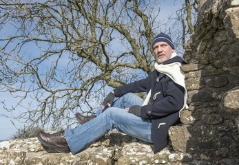 Fototapeta premium Mature man sitting on a stone wall in winter 