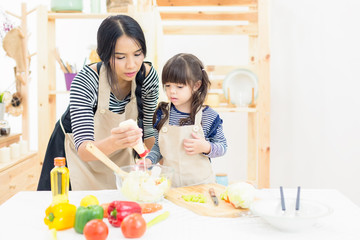 A little girl learning cooking practice with her Mom on salad bowl in kitchen background
