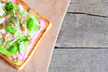 Sliced avocado, pumpkin seeds, lettuce, basil and beetroot sauce on a white bread toast. Breakfast sandwich on a wooden board and old wooden background with copy space for text. Tasty and healthy food