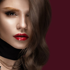 Fototapeta premium Beautiful girl with red lips and golden eyebrows, curls in Hollywood style. Beauty face. Photo taken in the studio.