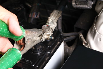 Man hand in action of doing jump start technic with car battery by using jump start cable in the scene focus to the cable forceps.