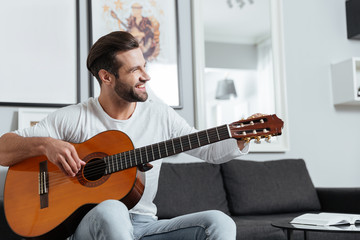 Happy man sitting on sofa playing on guitar