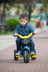 little boy ride toy motorcycle on sidewalk