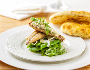 Smoked mackerel on a bed of green beans topped with sauce and rocket leaves.