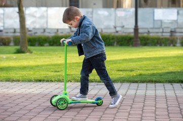 little boy learn to ride scooter in a park