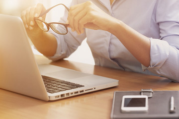 Business woman using laptop computer and holding glasses.
