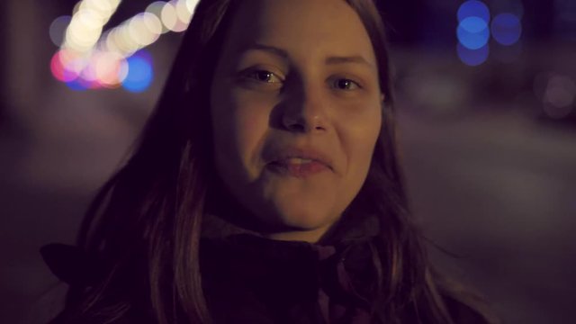 Portrait of a cute pensive smiling teen girl on a night city street. 4K UHD slowmo