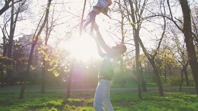 Young father throwing up his little daughter in the air and having fun in park, slow motion