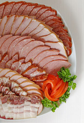 Meat cutting on a  plate background with a tomato rose and a sprig of parsley. Smoked meat, sausage...