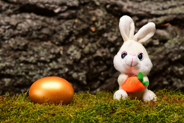 rabbit toy, golden easter egg on green moss, tree bark