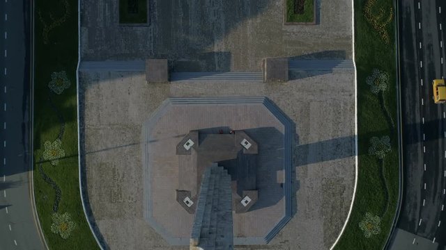 Drone camera flies backwards over the wings of victory memorial in 10th April Square. The camera is pointing directly down and then tilts up to show the Arkadia skyline