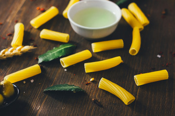 Tortiglioni pasta with bay leaves, olive oil and other ingredients on brown wooden surface.
