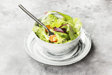The dietary mixed greens salad (mesclun, mache, lettuce) and cherry tomatoes in a bowl on a light...