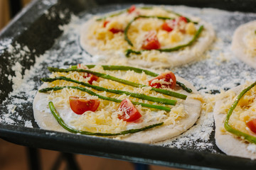 Cooking process of making mini pizza - small and personal, with cheese, tomatoes and asparagus.