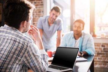 Obraz premium Young man using laptop while colleagues discussing project, small business meeting concept