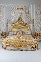 Luxury bedroom in light colors with golden furniture details. Big comfortable double royal bed in elegant classic interior