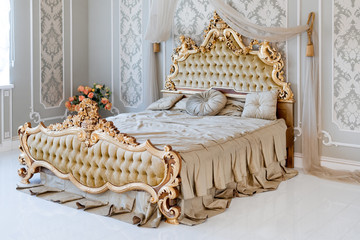 Luxury bedroom in light colors with golden furniture details. Big comfortable double royal bed in...
