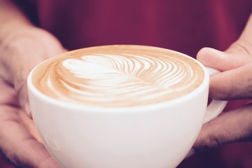 a cup of cappuccino coffee with beautiful latte art in man hands, wearing red t-shirt