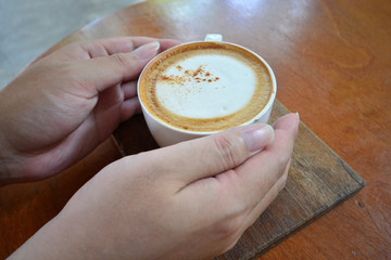 Female hand holding hot cup of coffee on wood table, Top view