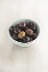 Black and green olives in a small bowl on a light wooden background