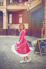 Beautiful dancing girl in a pink dress looks around the city street.