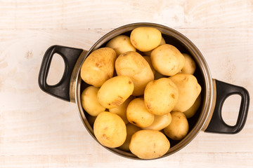 Flat lay young potatoes in the metal pot above wooden background