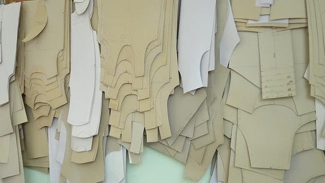 Many paper brown patterns for sewing clothes for babies and newborns of different sizes hanging on wall in sewing factory interior. Real time full hd video footage.
