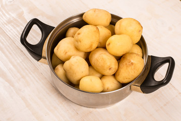 Full pot of young raw potatoes over wooden background