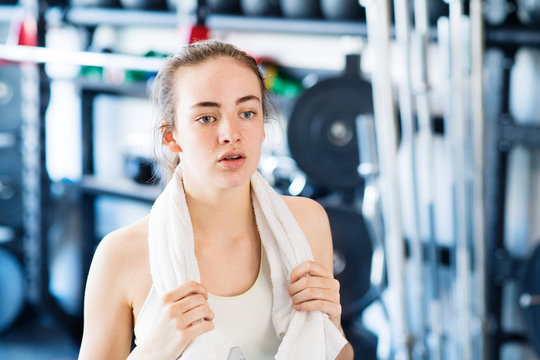 Young woman in gym, towel around her neck, resting