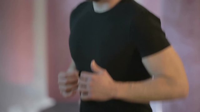 Giovane ragazzo vestito con maglia nera sta facendo riscaldamento in palestra con corsa sul posto