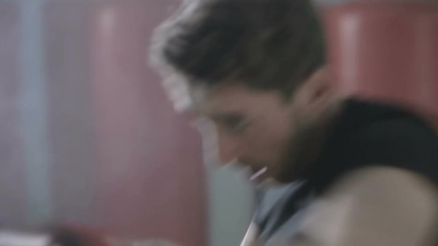 Giovane ragazzo si sta allenando al sacco da boxe in palestra con i guanti rossi e la maglia nera. Fumo bianco nello sfondo. 