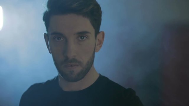 Ragazzo serio alza lo sguardo alla telecamera prima di allenarsi. Sfondo con luce blu e fumo bianco.
