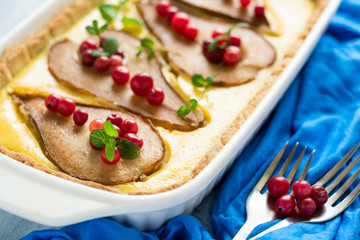Tart with roasted pears over rikotta cream decorated cranberries and mint leaves on blue wooden table. Selective focus