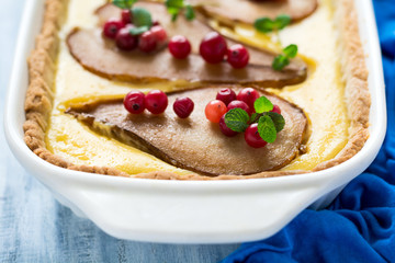 Tart with roasted pears over rikotta cream decorated cranberries and mint leaves on blue wooden table. Selective focus