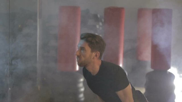 Ragazzo giovane con maglia nera si sta allenando in palestra con la kettlebell  giallo. Fumo per sfondo.