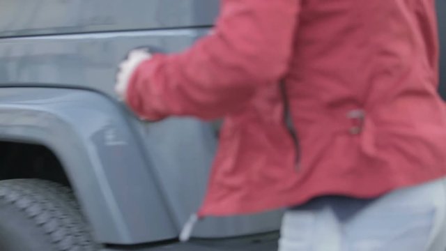 Ragazzo con giacca rossa sta posando il borsone sportivo nel bagagliaio della sua automobile.