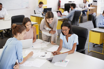 Four young businesswomen working at desk in open plan office