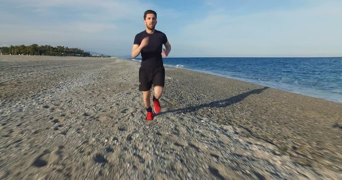 Giovane ragazzo si allena alla corsa in riva al mare con maglietta e pantaloni neri e scarpe rosse.