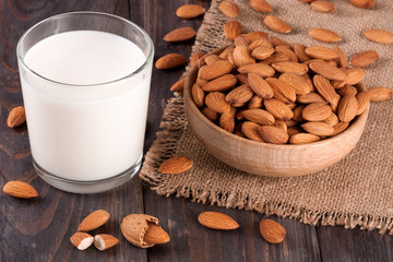 Almond milk in a glass and almonds in a bowl on dark wooden background