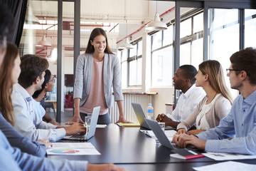 Fototapeta premium Woman addressing team leans on desk at business meeting