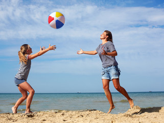 Happy parent and child play a ball at coast on a sunny summer day. Beach sports