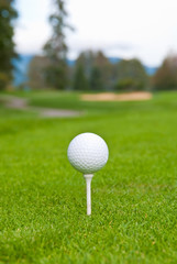 Golf ball on tee over a blurred green, bunker and path. Shallow depth of field. Focus on the ball.