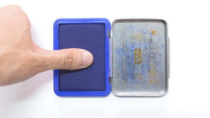 Finger on blue ink stamp pad in front of a white background